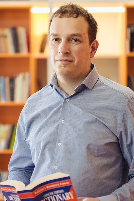Dmitri Šmorgun hoiab käes avatud inglise keele sõnaraamatut, taustal raamaturiiul